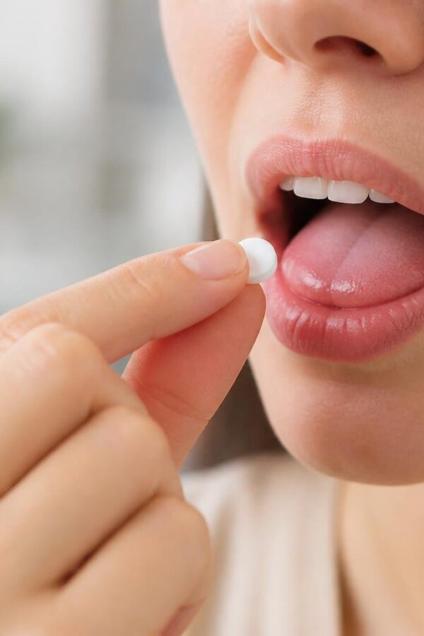 Pessoa segurando um comprimido sublingual próximo à boca, prestes a colocá-lo sob a língua.